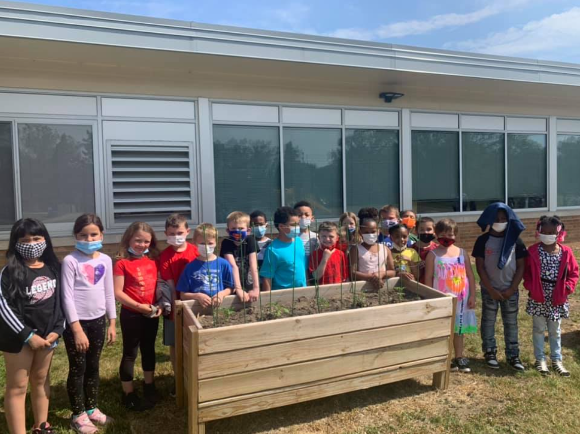 Minges Brook Elementary students stand by a raised bed containing seeds they planted.
