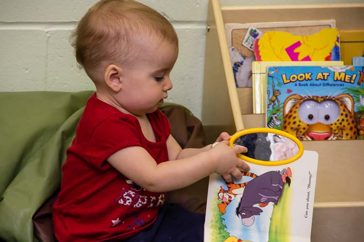 A toddler explores a book at Take-A-Break Childcare. Photo by Susan Andress
