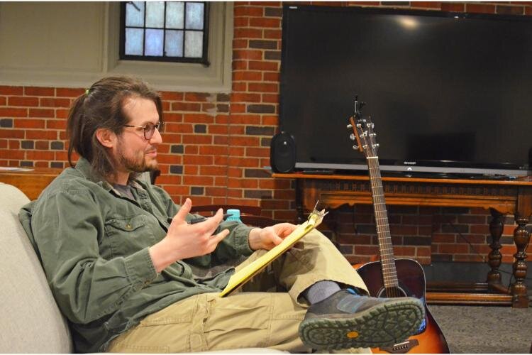 Josh Jerz speaks to the group as facilitator and fiddles on his guitar while the conversation ebbs and flows.