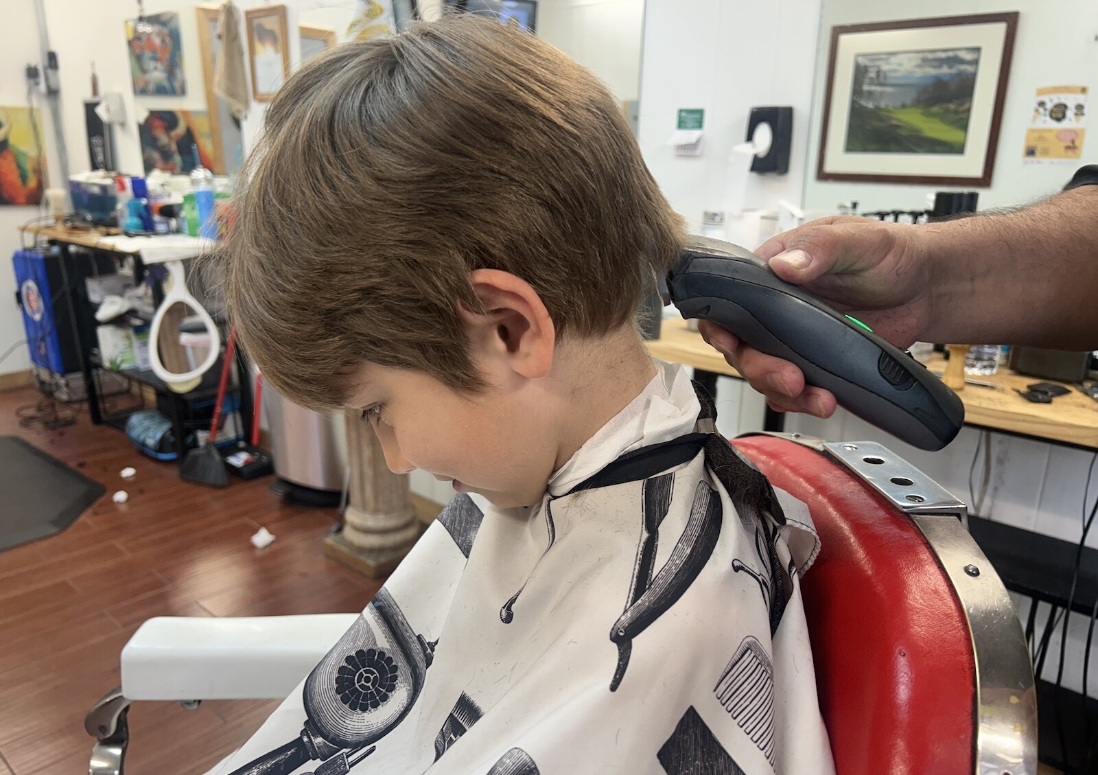 A young boy gets his haircut by Robert DeAnda, owner of Rob’s Barber Shop during a Barbershop and Literacy event in the Vine Neighborhood.