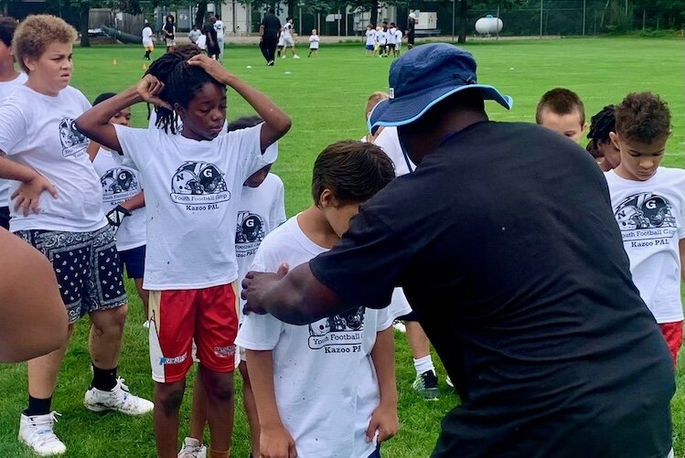 A coach helps a youngster do football drills at the Kalamazoo Youth Football Camp, held Saturday, Aug. 26, 2025 at Mayor’s Riverfront Park.